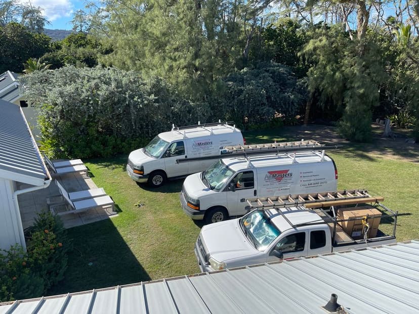 Two service vans parked in a grassy area near a house surrounded by trees.