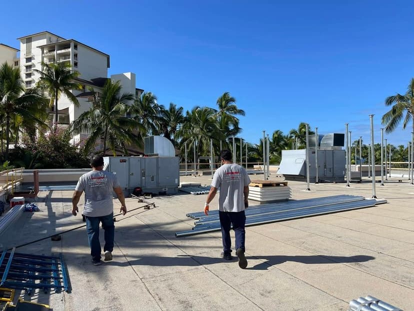 Workers on a rooftop construction site with metal materials and palm trees in the background.
